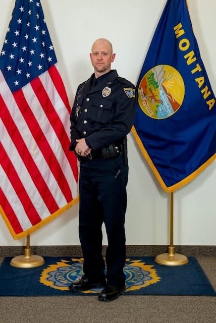 Scott Rouse as a police officer standing in front of the US and Montana flag